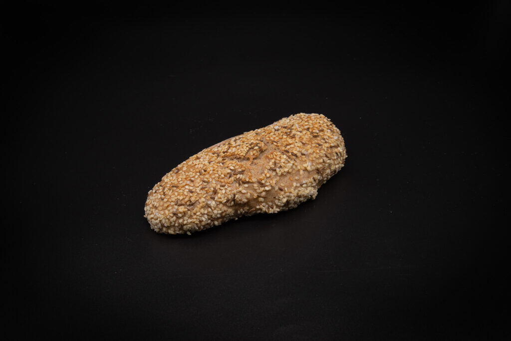 Ein einzelner, mit Sesam bestreuter Brotlaib auf einem schlichten schwarzen Hintergrund.
