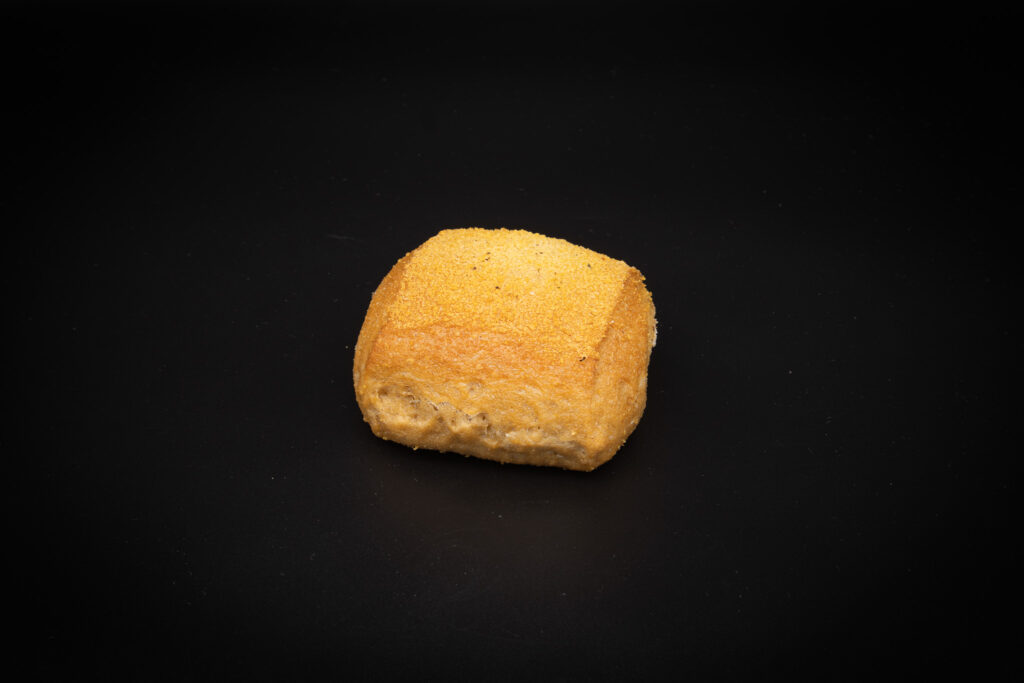 Ein einzelnes quadratisches Brötchen mit einer goldenen Kruste liegt auf einem schlichten schwarzen Hintergrund.