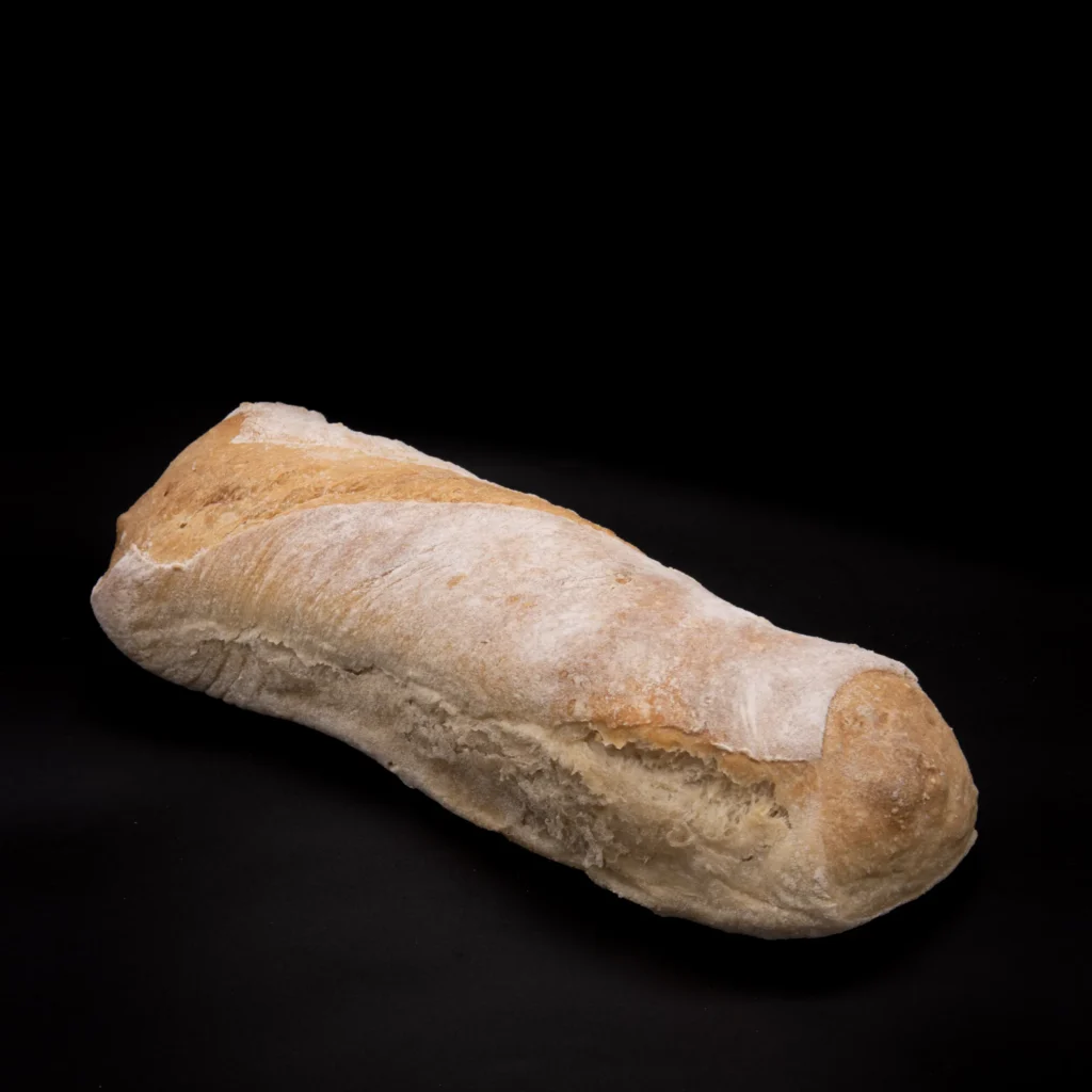 Ein Laib rustikales, knuspriges Brot mit Mehl bestäubt liegt auf einem schwarzen Hintergrund.