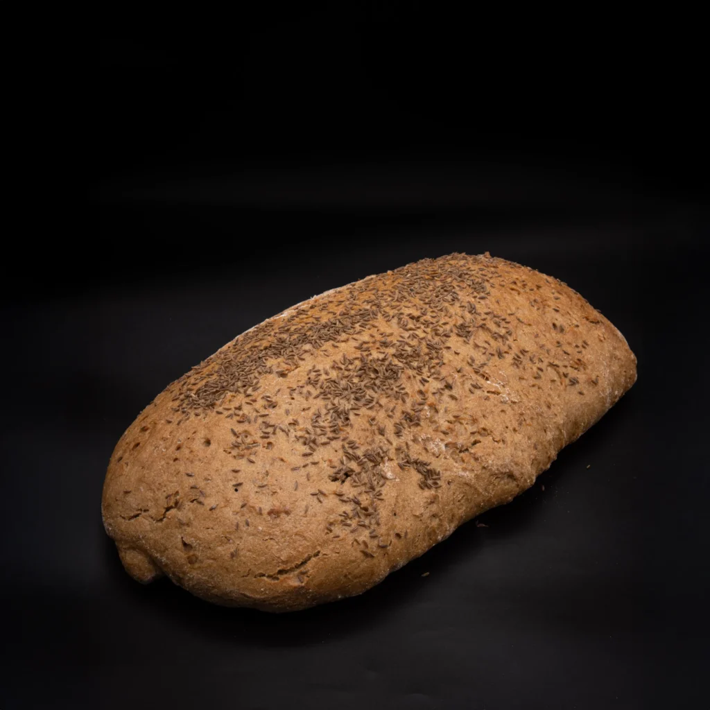 Ein mit Kümmel belegter Laib Schwarzbrot auf schwarzem Hintergrund.