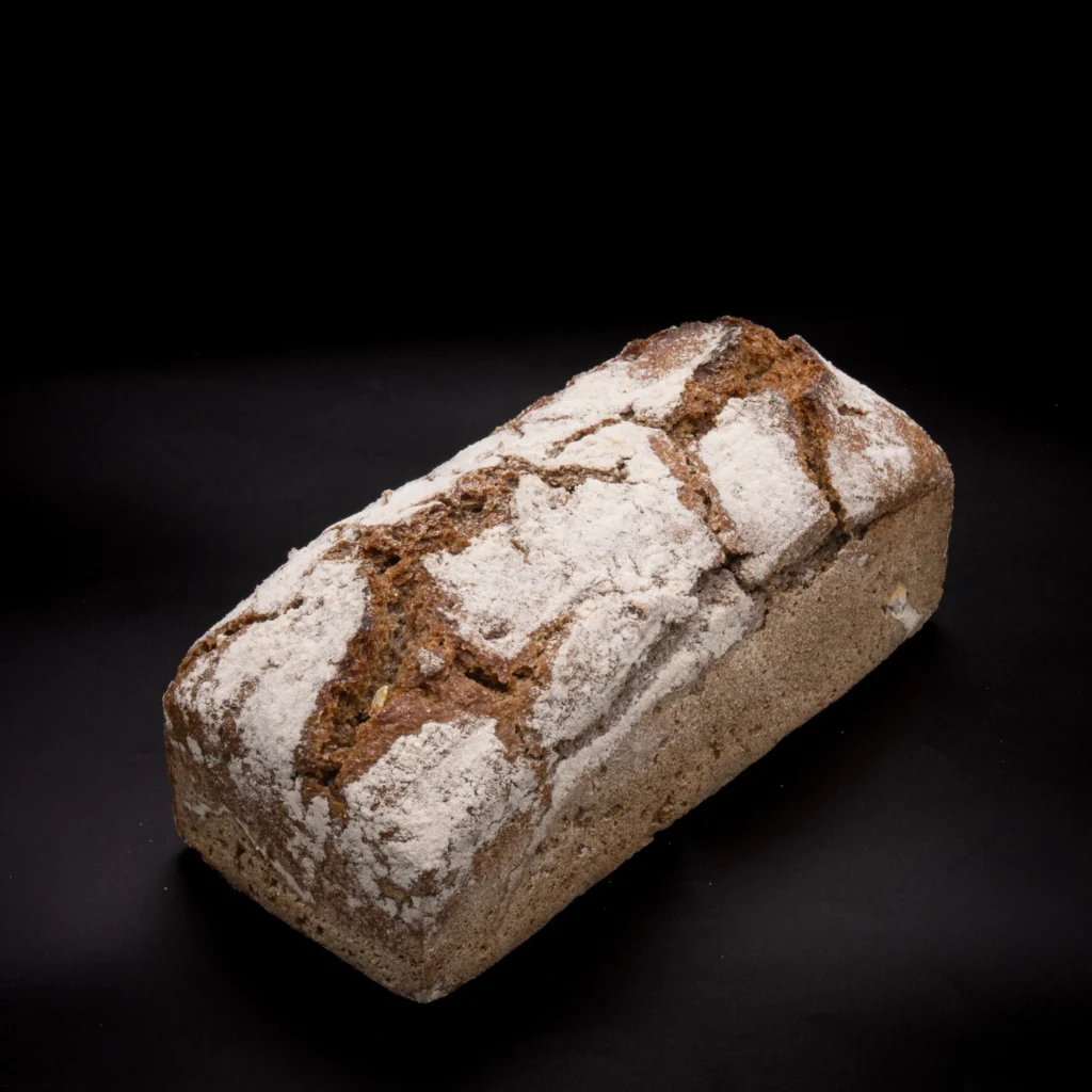 Ein Laib rustikales Brot mit einer rissigen, mehlbestäubten Kruste liegt auf einem schwarzen Hintergrund.