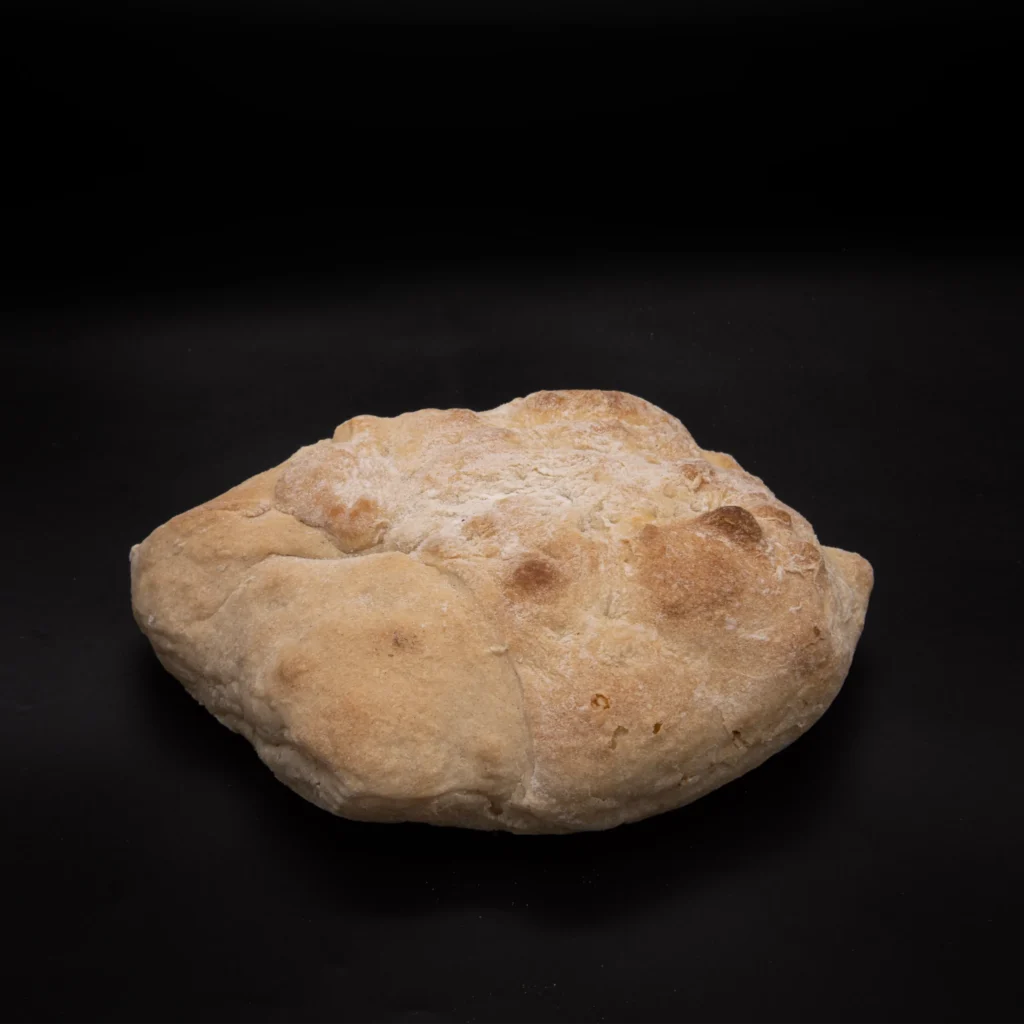 Ein runder, rustikaler Brotlaib mit goldbrauner Kruste steht auf einem schwarzen Hintergrund.