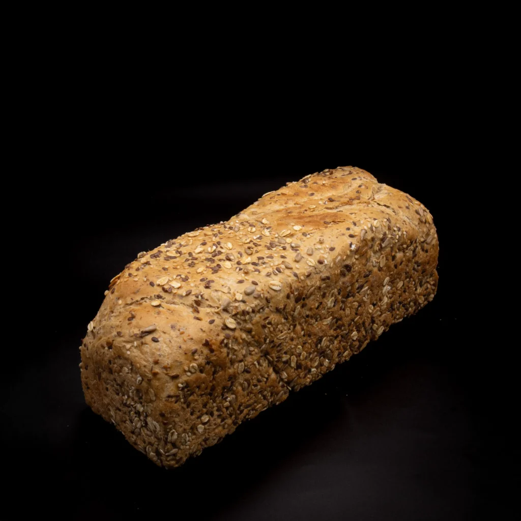 Ein Laib Mehrkornbrot mit sichtbaren Körnern und Haferflocken auf der Kruste, platziert auf einem schlichten schwarzen Hintergrund.