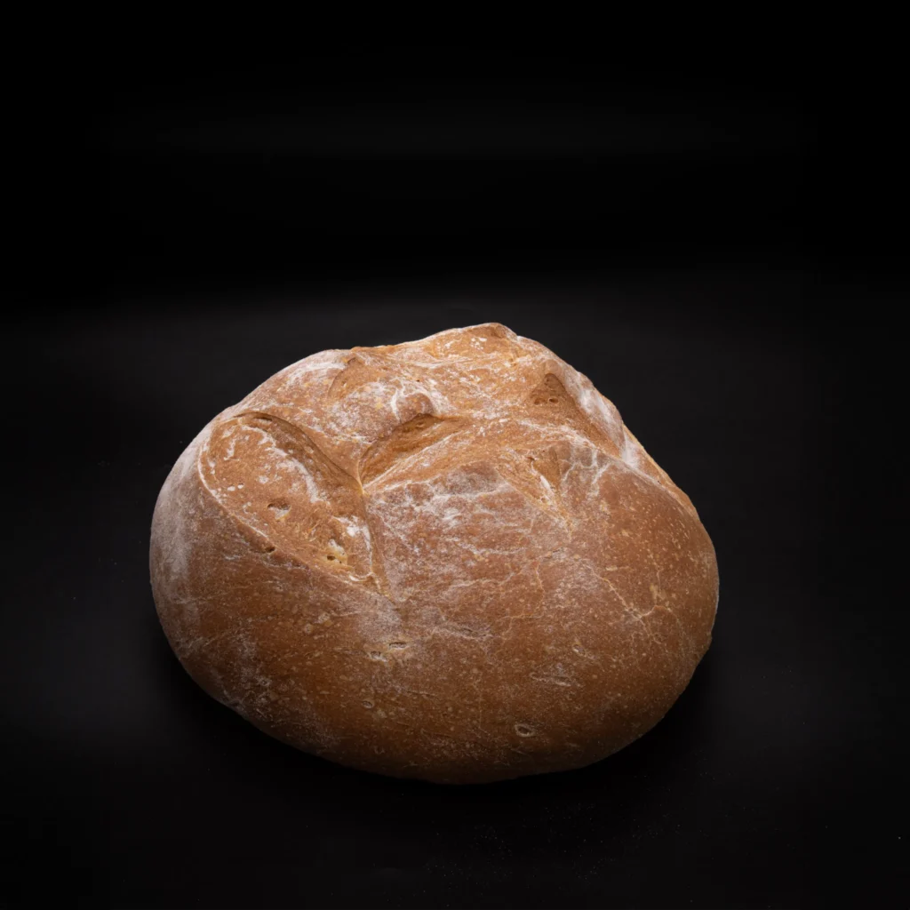 Ein runder, rustikaler Brotlaib mit goldbrauner Kruste steht auf einem schwarzen Hintergrund.