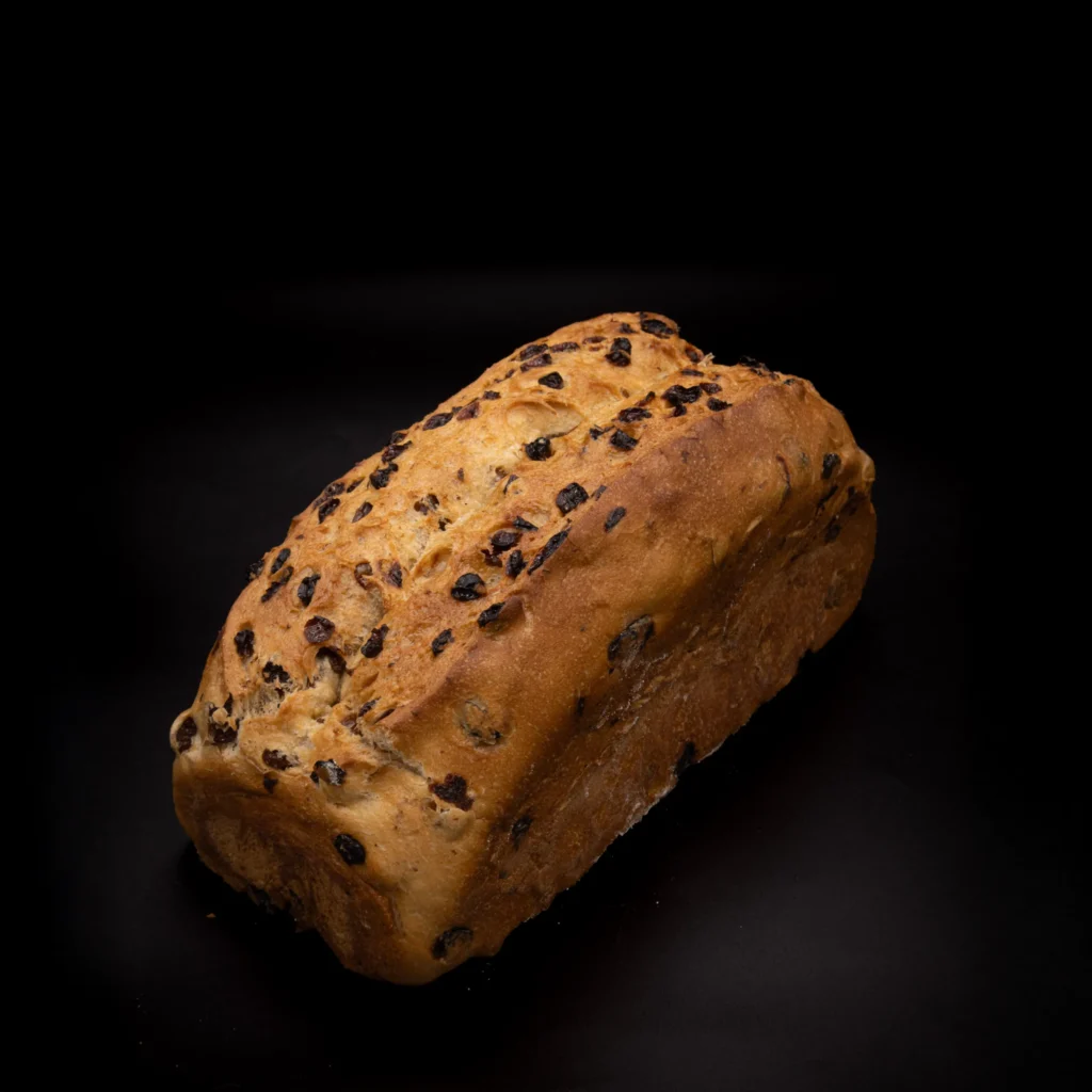 Ein Rosinenbrot mit goldbrauner Kruste ist auf einem schwarzen Hintergrund platziert, der seine Textur und die verstreuten Rosinen hervorhebt.