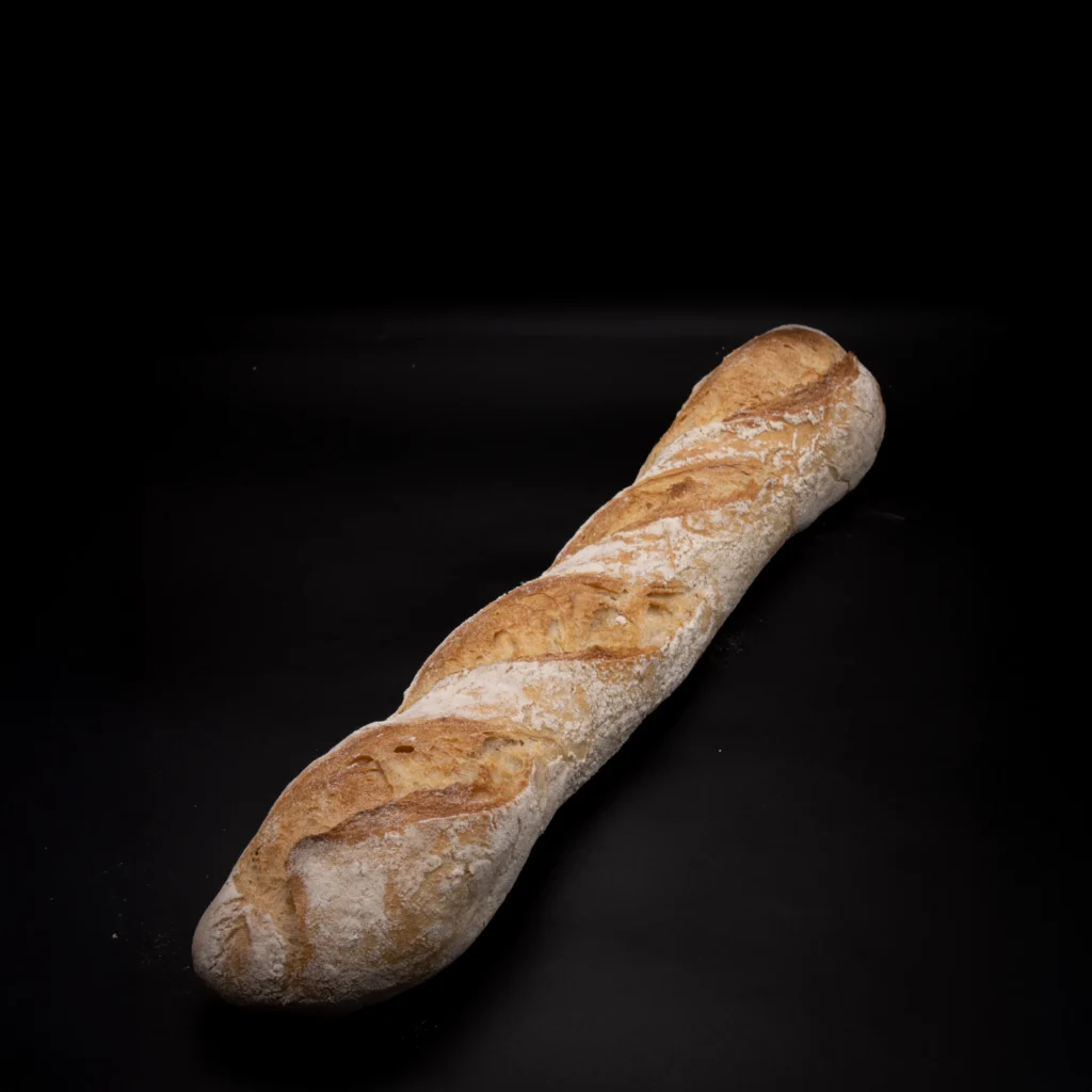 Ein einzelnes Baguette mit goldbrauner Kruste und Schlitzen auf der Oberseite ist auf einem schwarzen Hintergrund platziert.