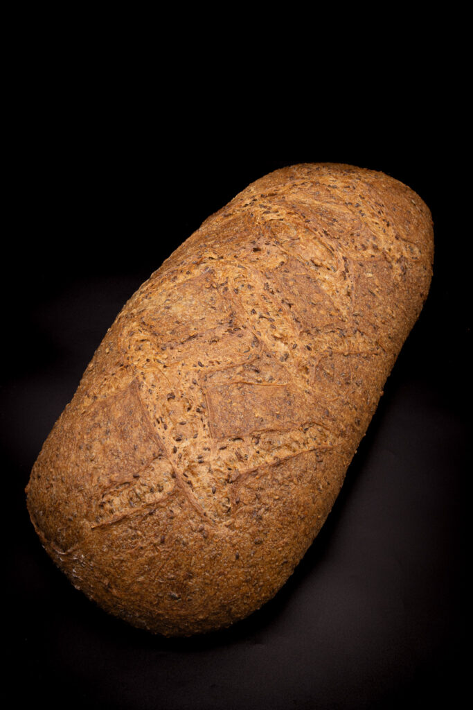 Ein Laib Vollkornbrot mit einer strukturierten, braunen Kruste liegt auf einem schwarzen Hintergrund.